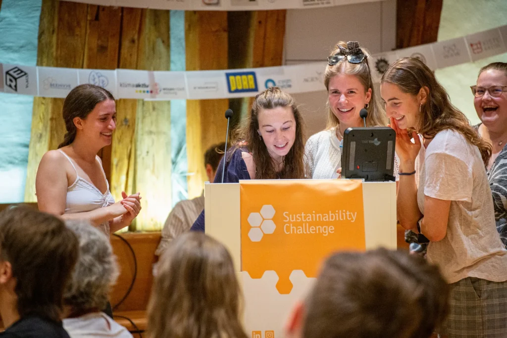 Four students laughing together at a Sustainability Challenge lectern while presenting their project